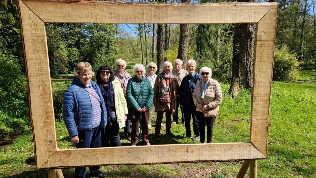 9 members of the Garden Visits group pose behind a viewing frame at Evenley Wood Garden